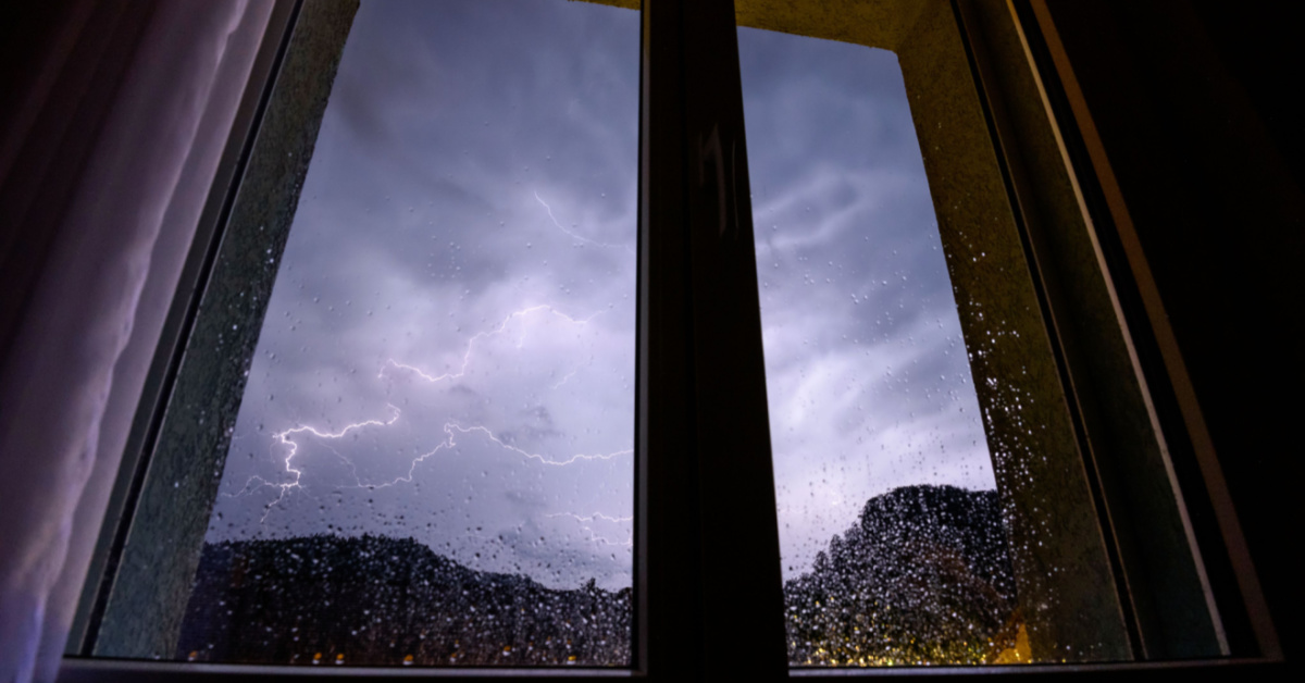 Interior home, looking out on a storm through a patio door or a tall window. Protect your home windows from natural disasters with 3M window film.
